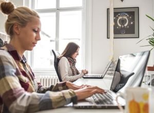 an image looking across a desk, where two women are looking at laptops