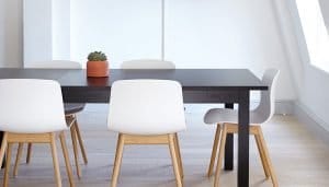a black wooden table with a plant in a ceramic pot on it surrounded by white chairs with light wooden legs