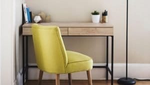 a mustard coloured chair pulled out from a simple wooden desk with a black metal frame
